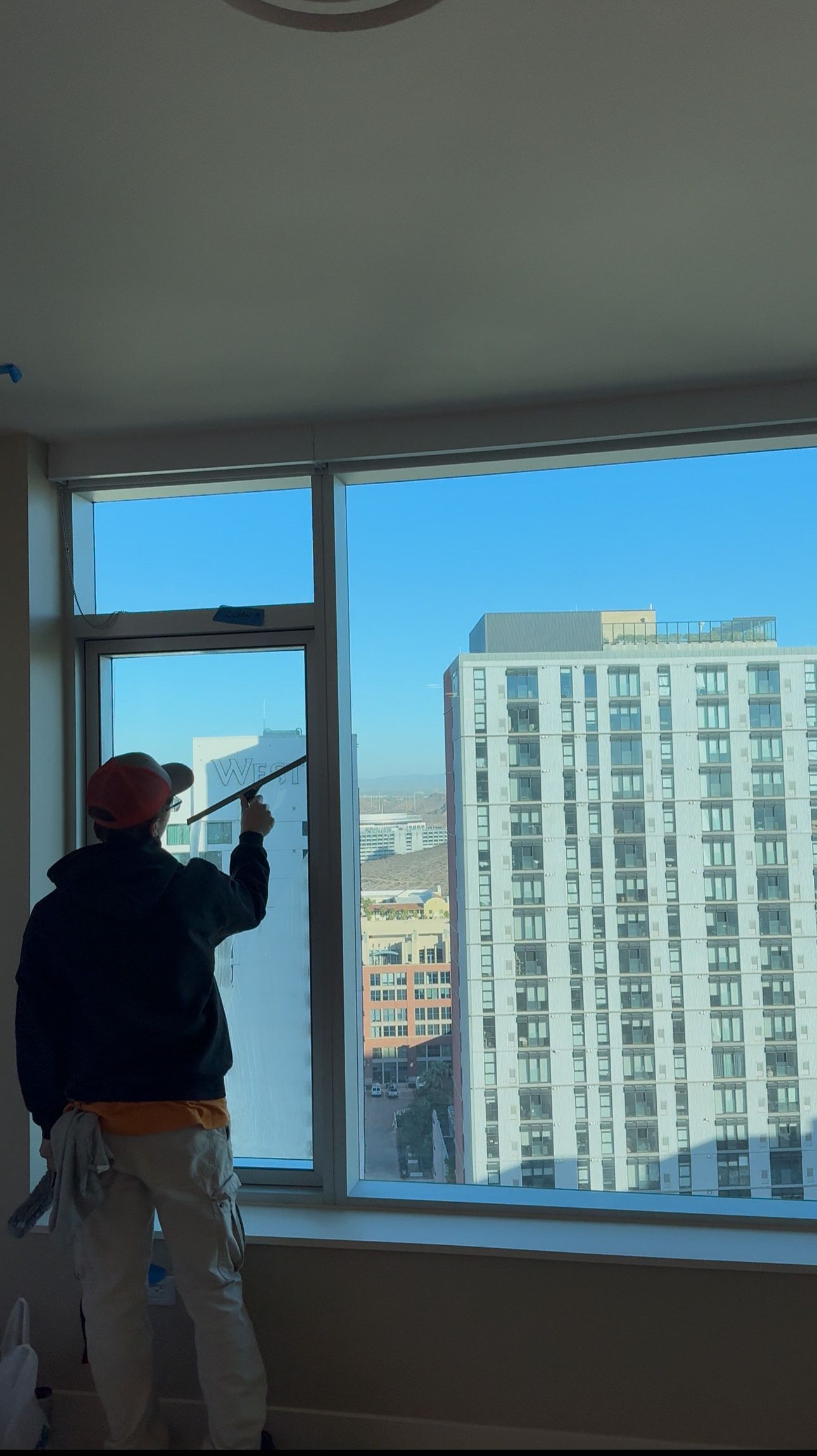 A man is cleaning a window in a room with a view of a city.