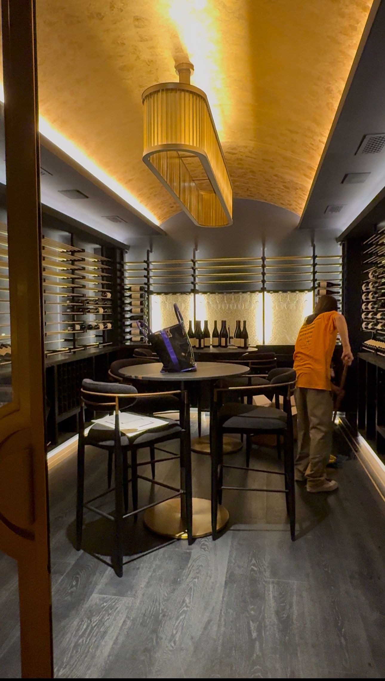 A man in an orange shirt is standing in a room with tables and chairs.