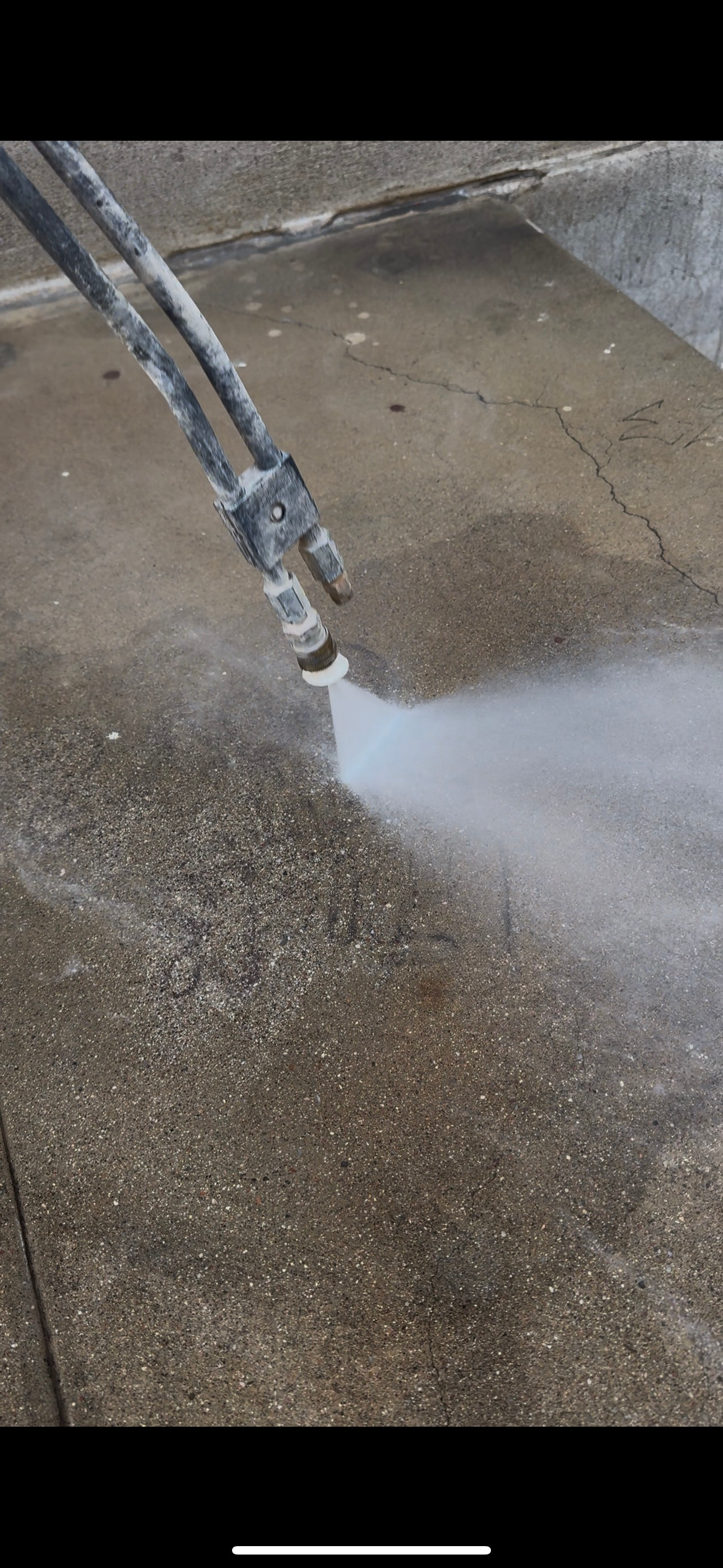 A power washer spraying water onto a concrete surface.