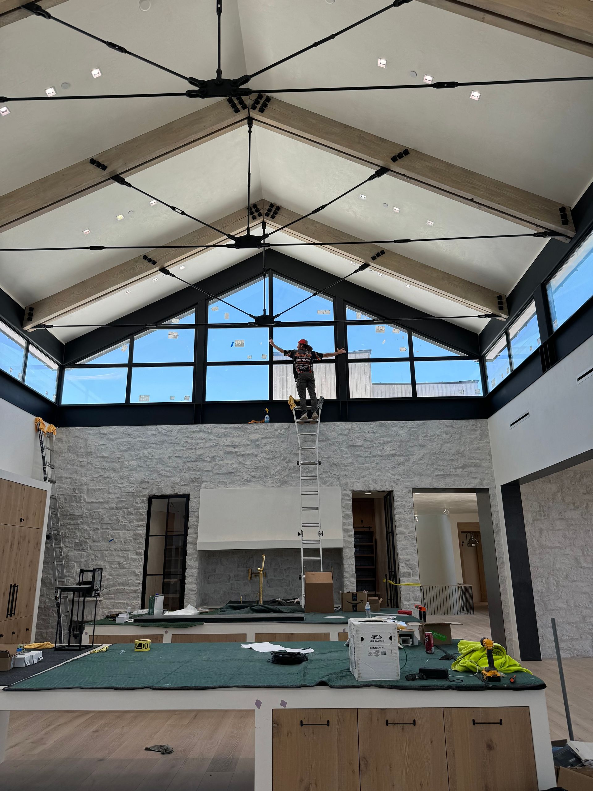 A man is standing on a ladder in a large room with a ceiling fan.