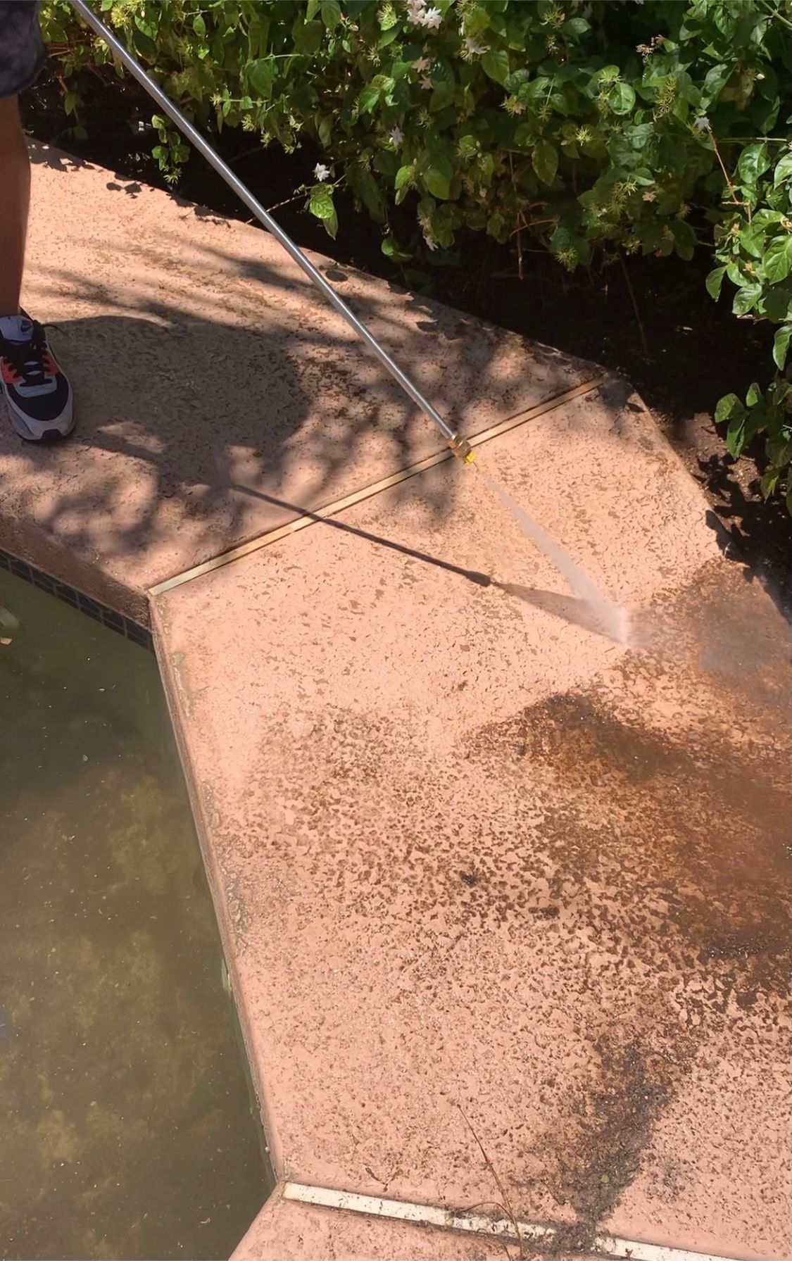 A person is cleaning a sidewalk with a high pressure washer.