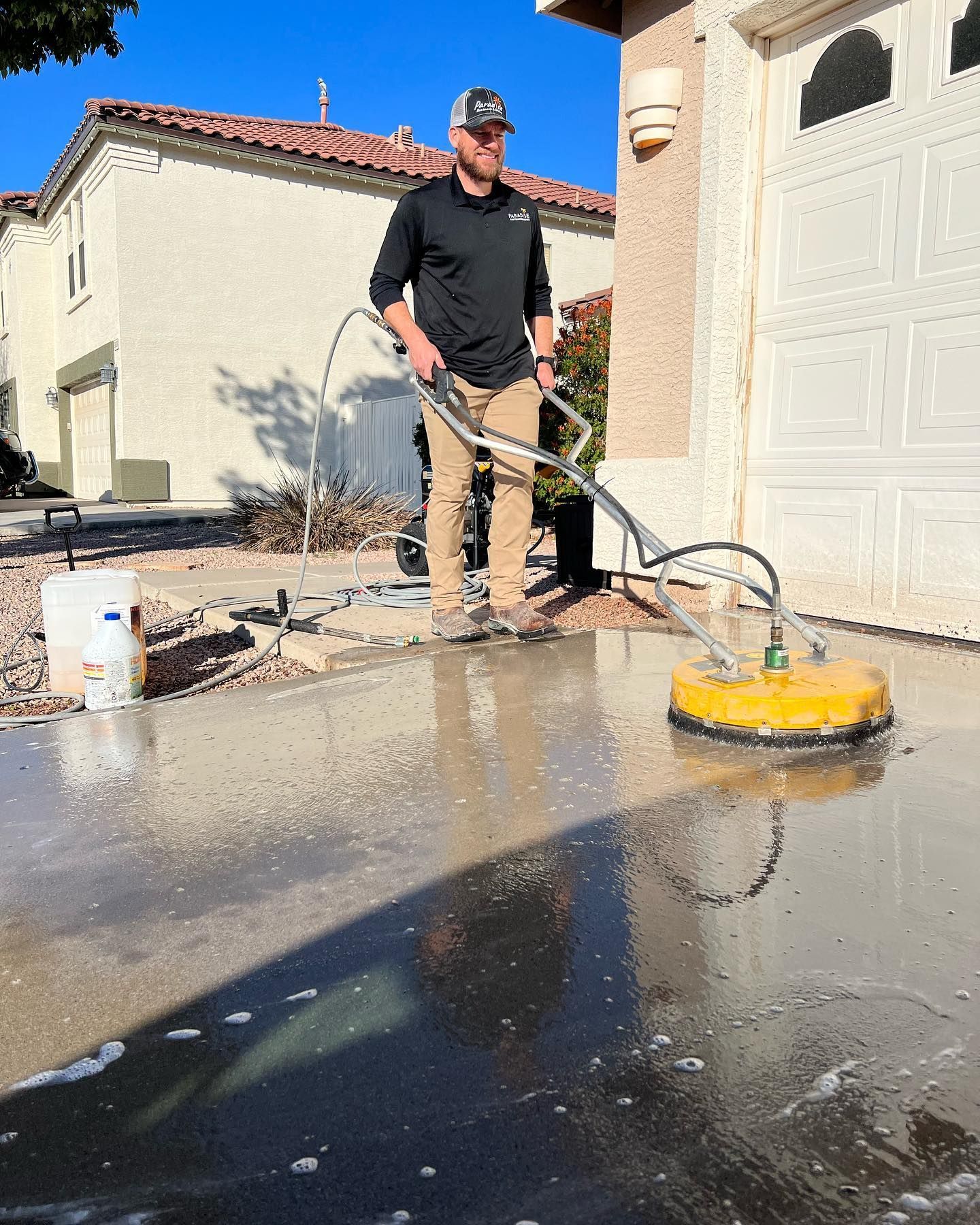 A man is cleaning a concrete driveway with a machine.