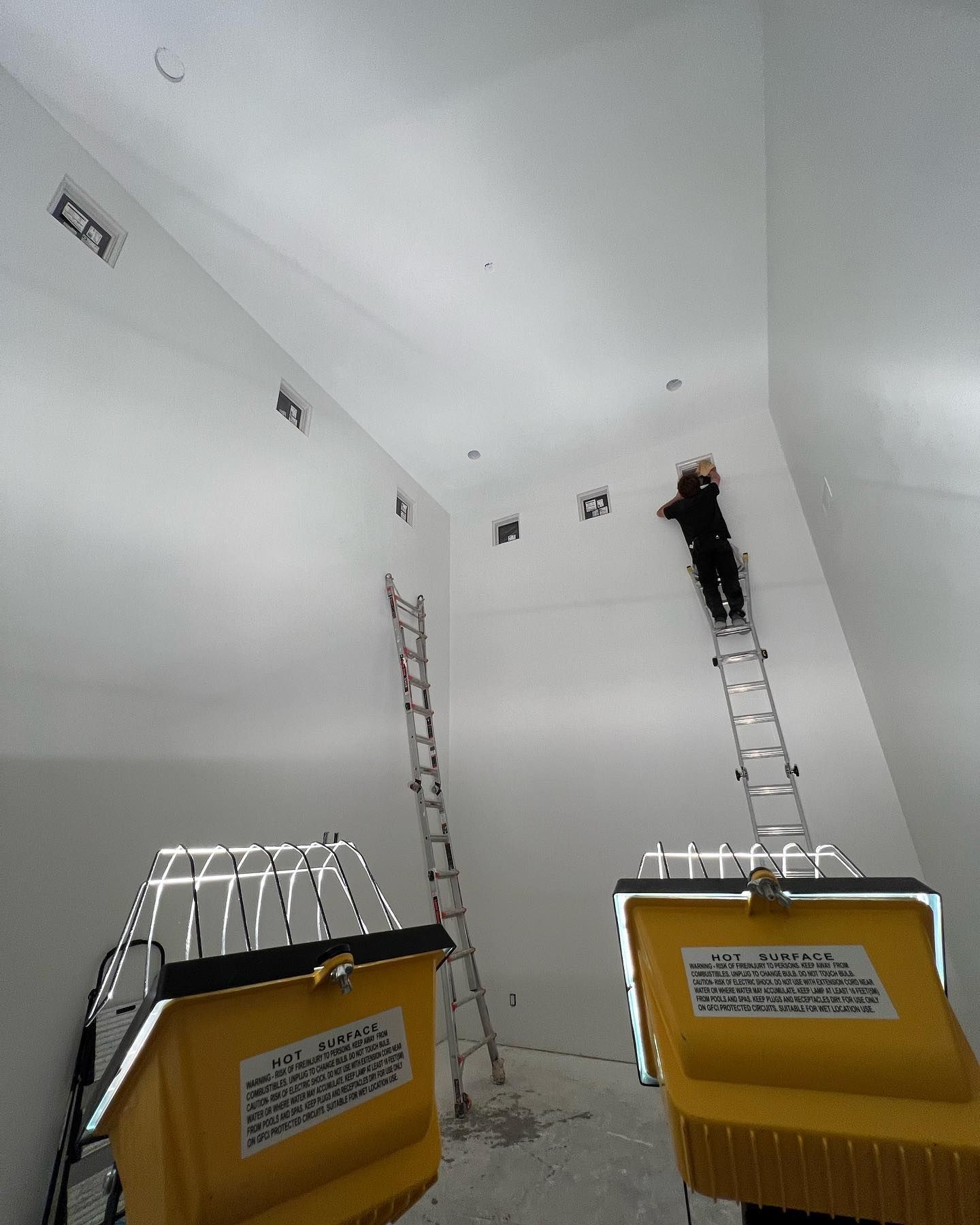 A man is standing on a ladder in a room with two yellow bins