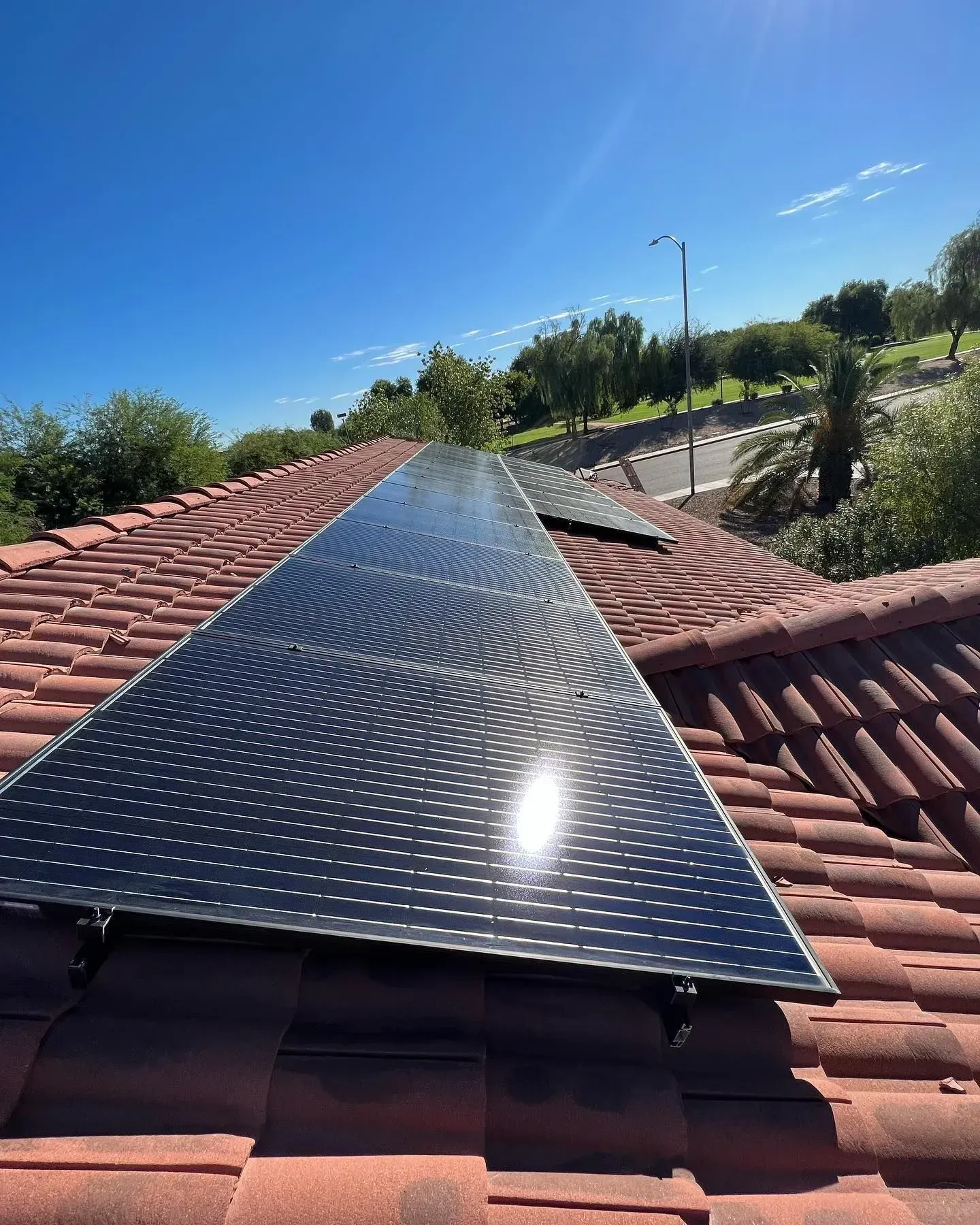 Solar panels on a red tile roof, bright sun, clear blue sky.