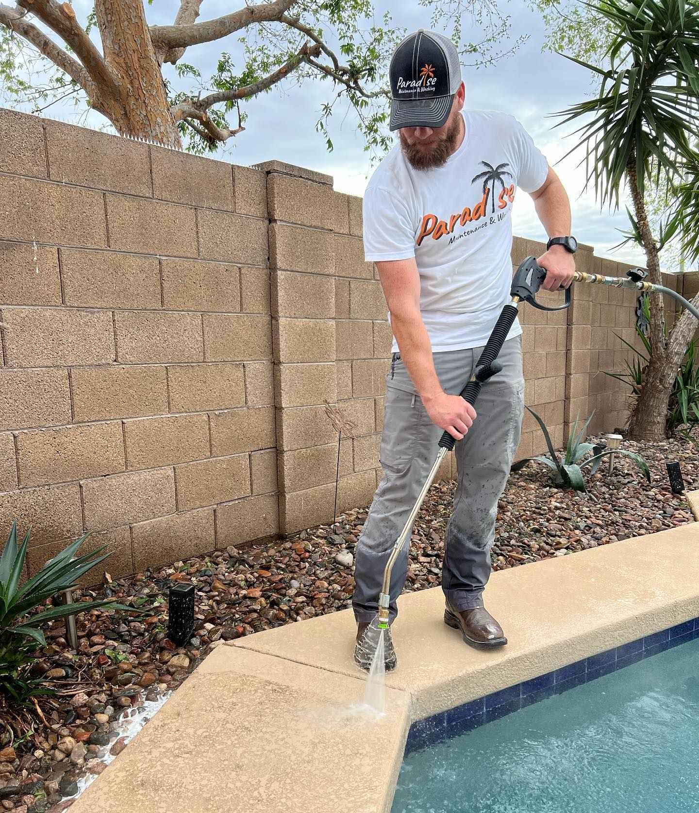 A man is cleaning the side of a pool with a hose.