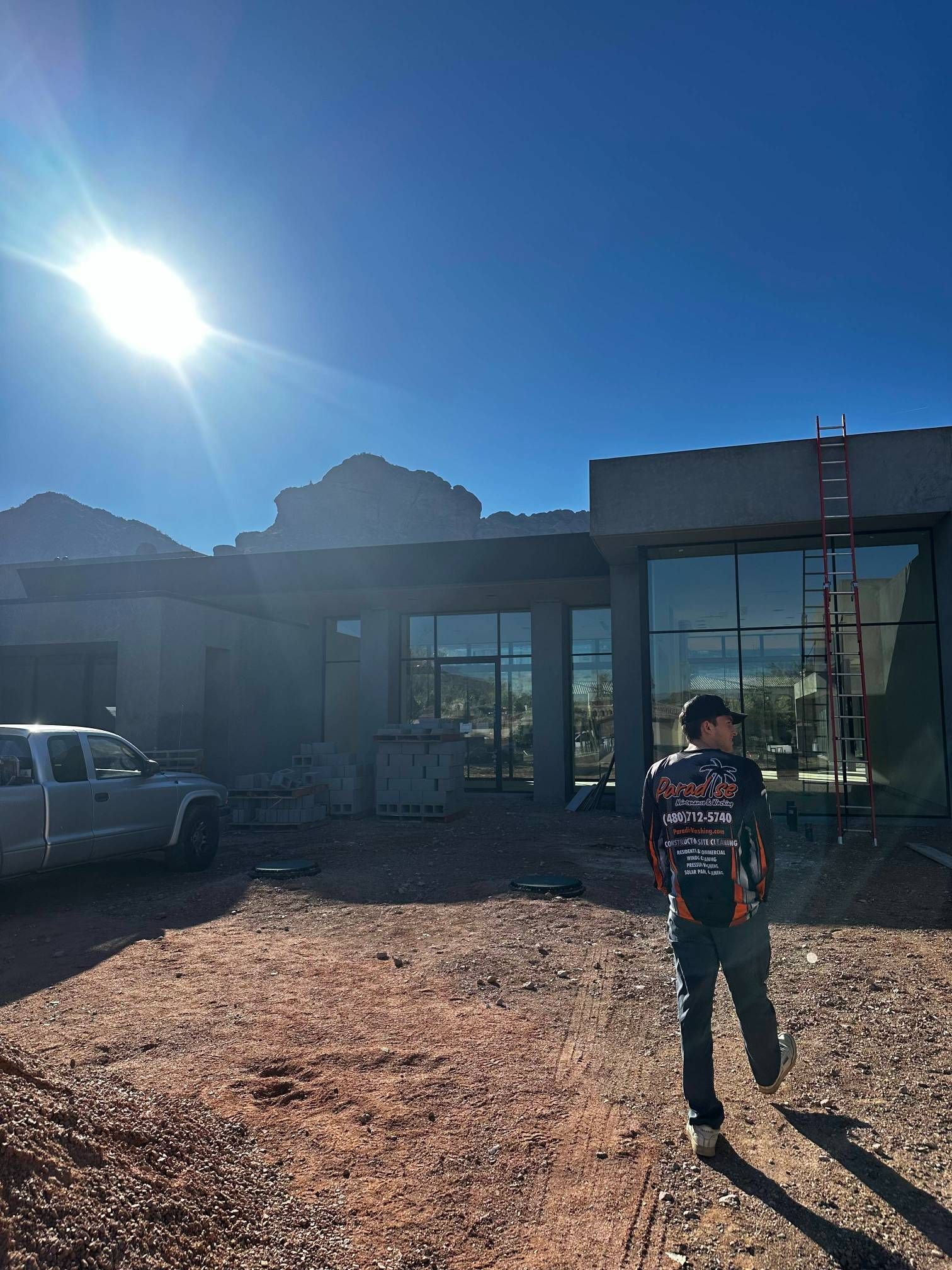 Person walking towards a modern home under construction on a sunny day. A truck is parked to the left.