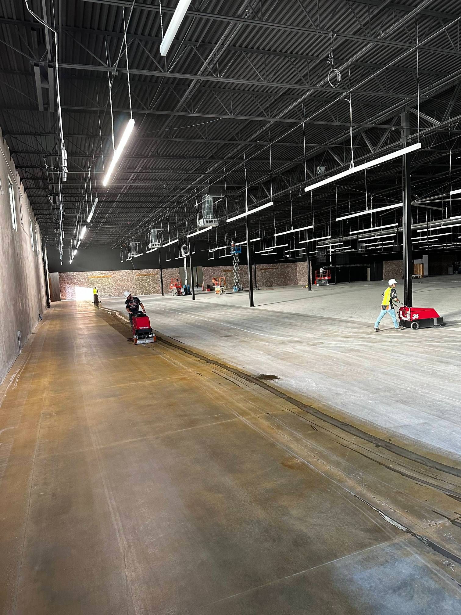 Large industrial space being cleaned; two workers operate floor scrubbers.