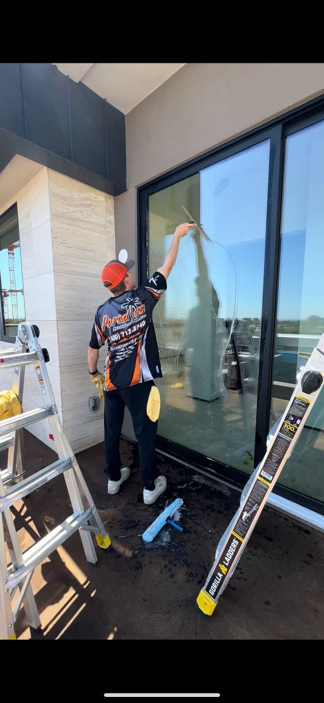 A person cleaning a large window on a balcony, using a squeegee.