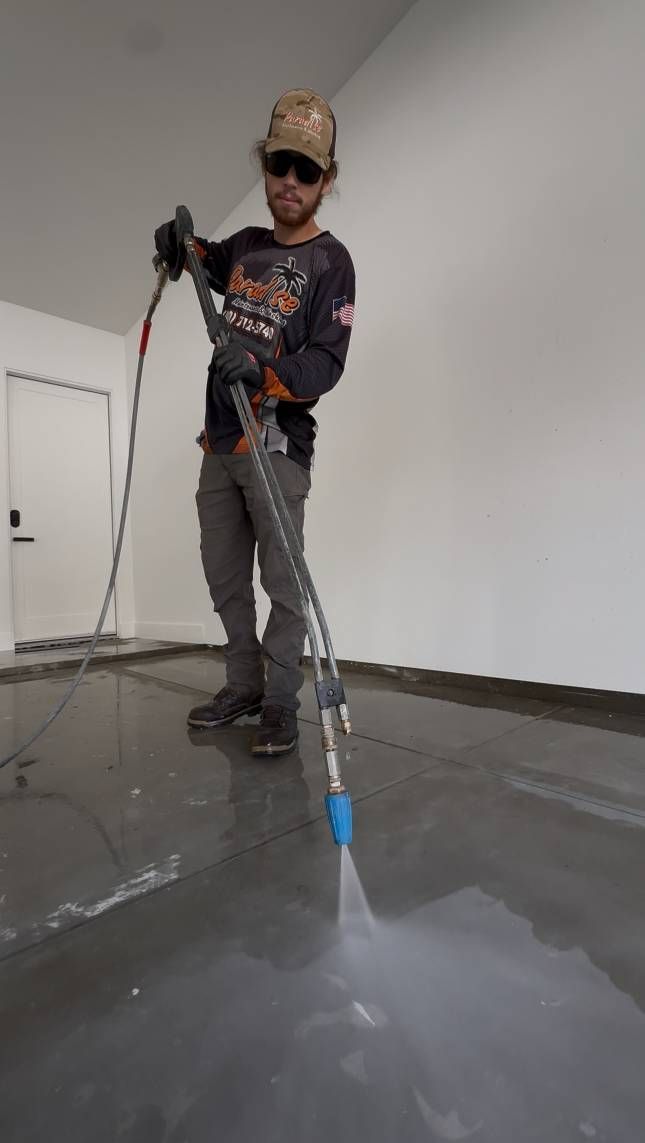Person pressure washing a concrete floor in a room.