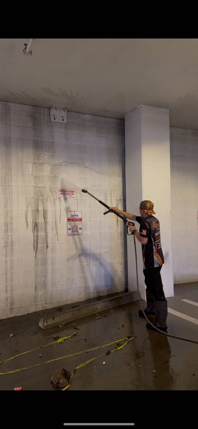 A person power washing graffiti off a concrete wall. The setting appears to be an urban area.