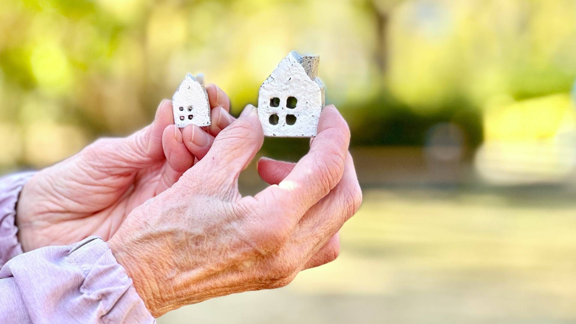 An elderly woman is holding two small houses in her hands.