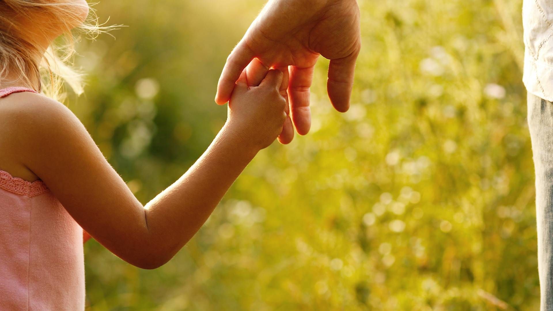 A little girl is holding a man 's hand in a field.