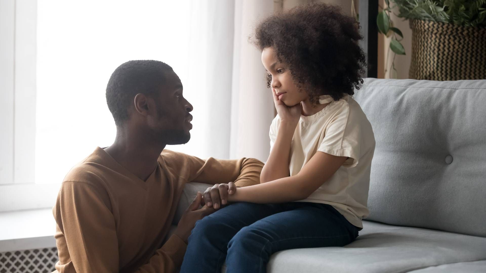 A man and a little girl are sitting on a couch talking to each other.