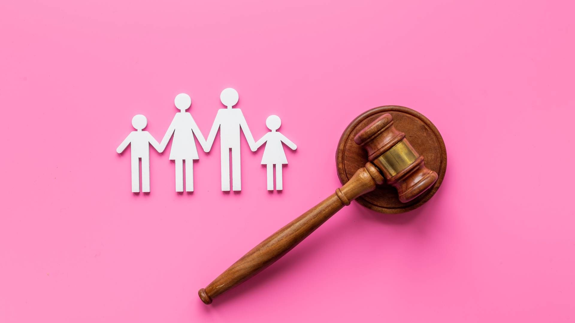A wooden judge 's gavel and a paper cut out of a family on a pink background.