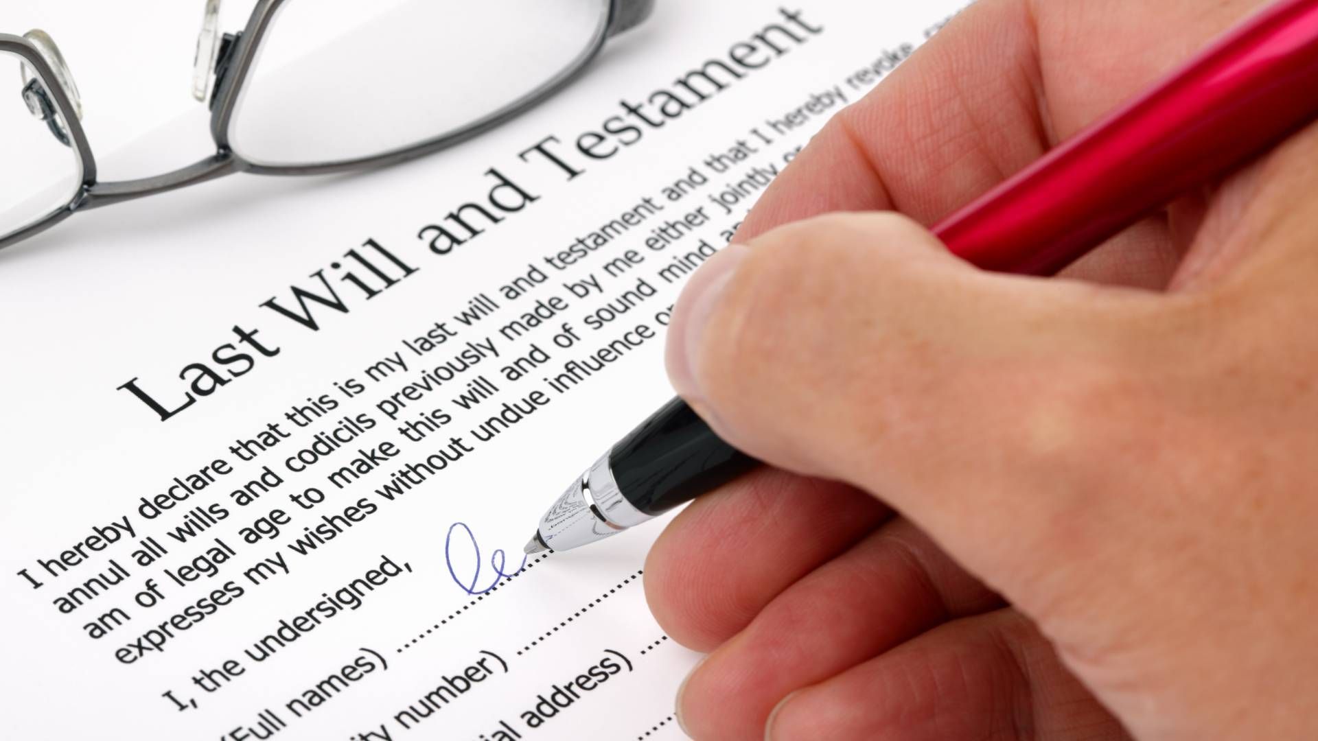 A person is signing a last will and testament with glasses in the background.