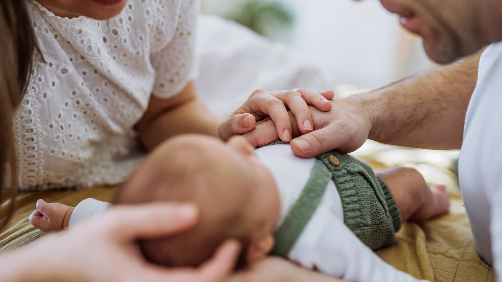 A man and a woman are holding a baby 's hand while laying on a bed.