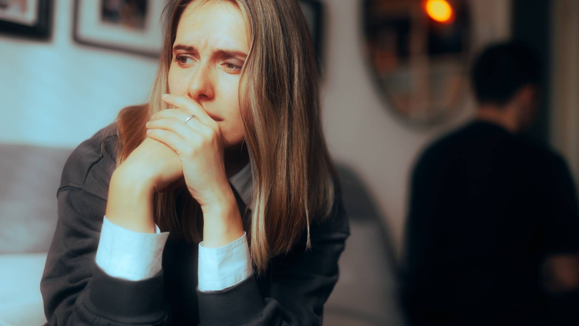 A woman is sitting on a couch with her hands on her face.