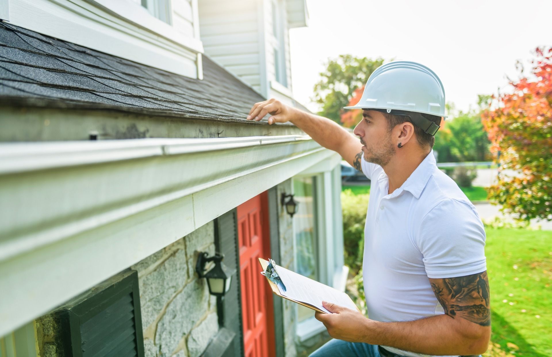 A man in a hard hat is looking at the gutter of a house for water damage.
