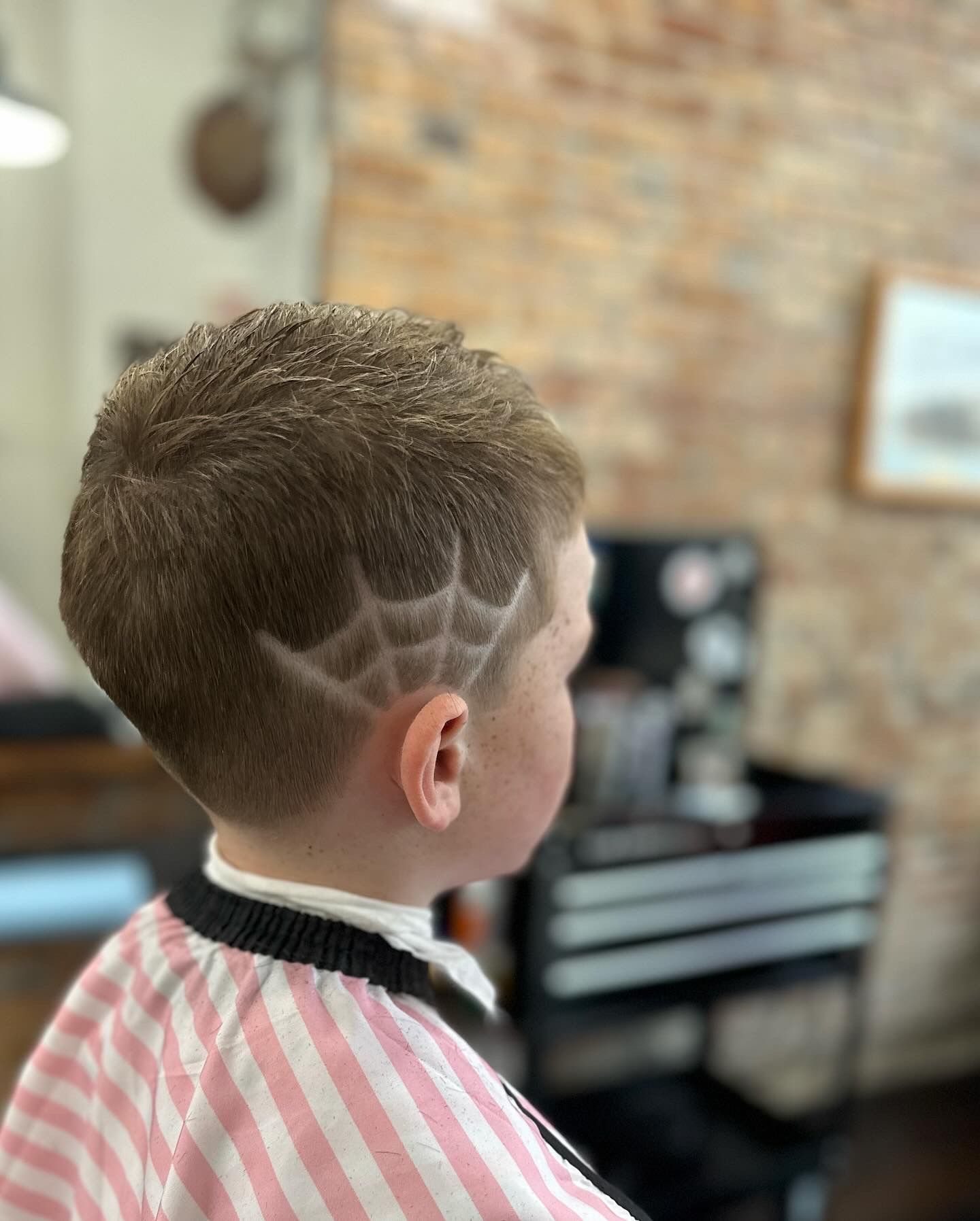 Child with a spiderweb haircut on a textured background. The child is wearing a barber's cape.