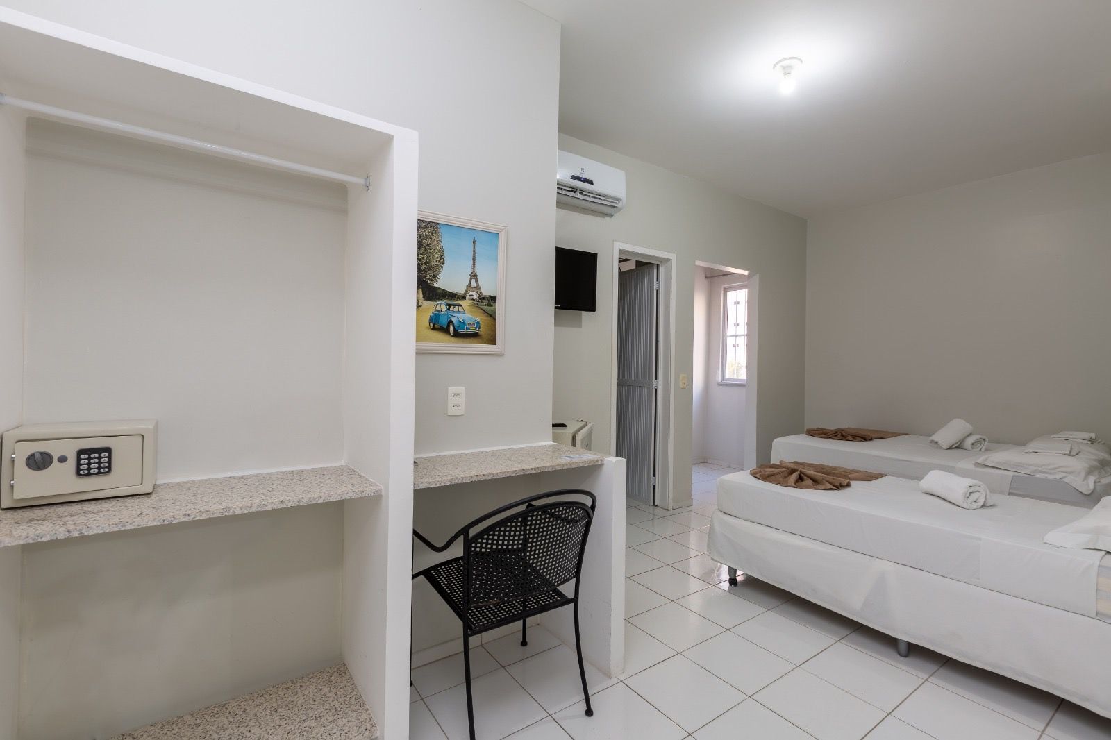 Um quarto de hotel com duas camas de cama feitas de branco, uma escrivaninha com uma cadeira preta e um closet aberto contendo um pequeno cofre embutido na parede.