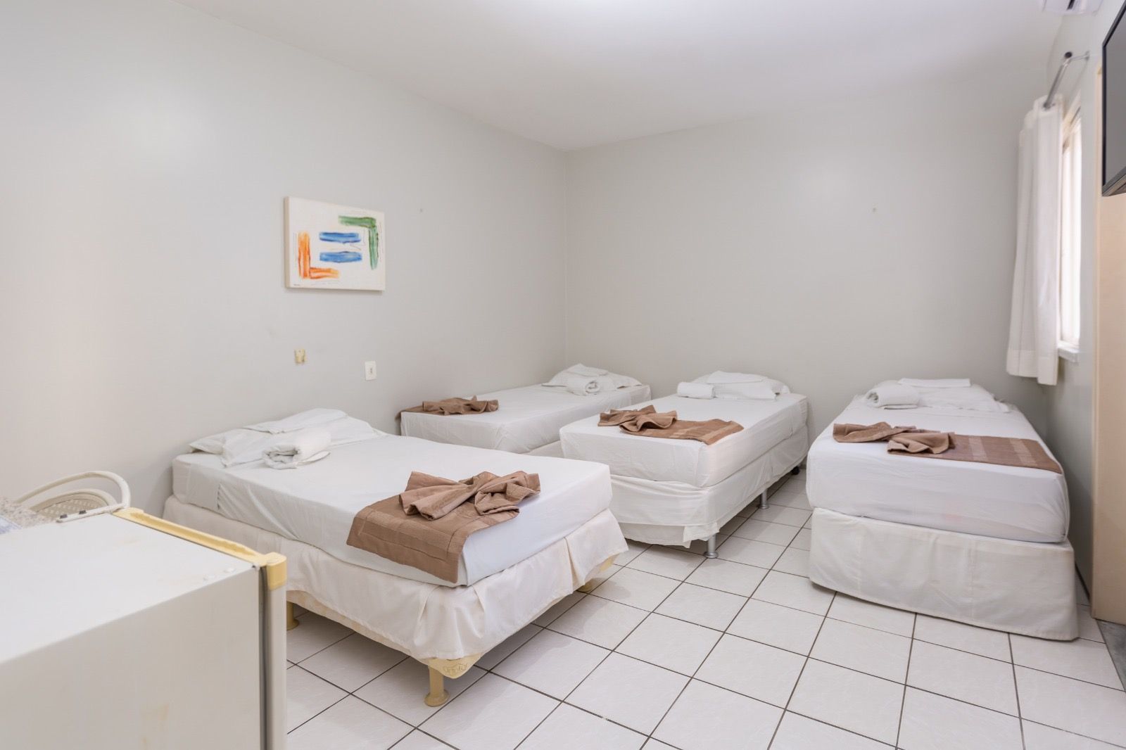 Um quarto de hotel com quatro camas de solteiro enfileiradas, com roupa de cama branca e piso de azulejo.