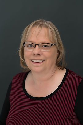 A woman wearing glasses and a striped shirt is smiling for the camera.