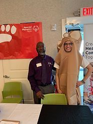 A man in a teddy bear costume is standing next to a man in a purple shirt.
