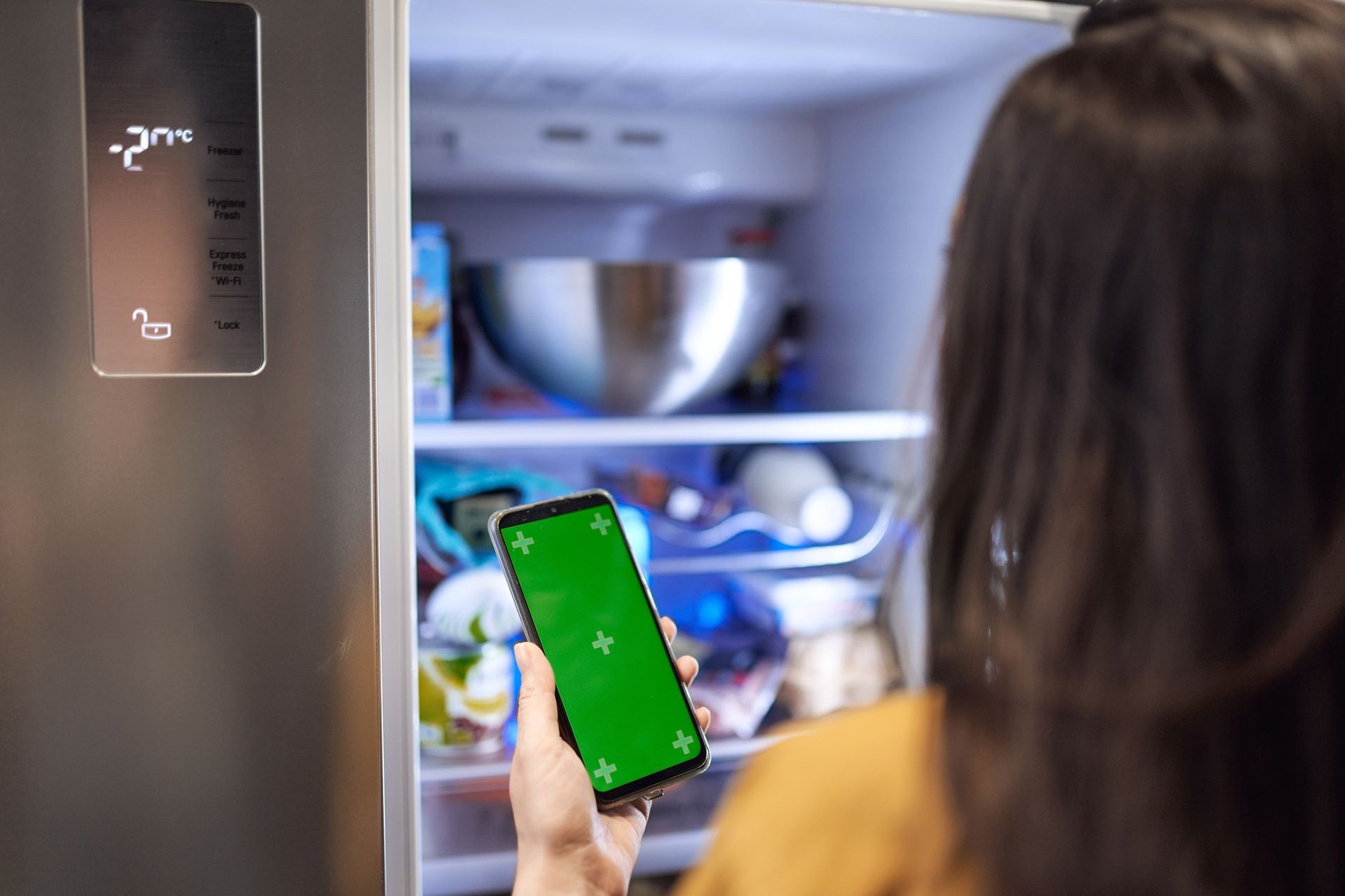 Back view of crop unrecognizable female standing in front of modern fridge with opened door and usin