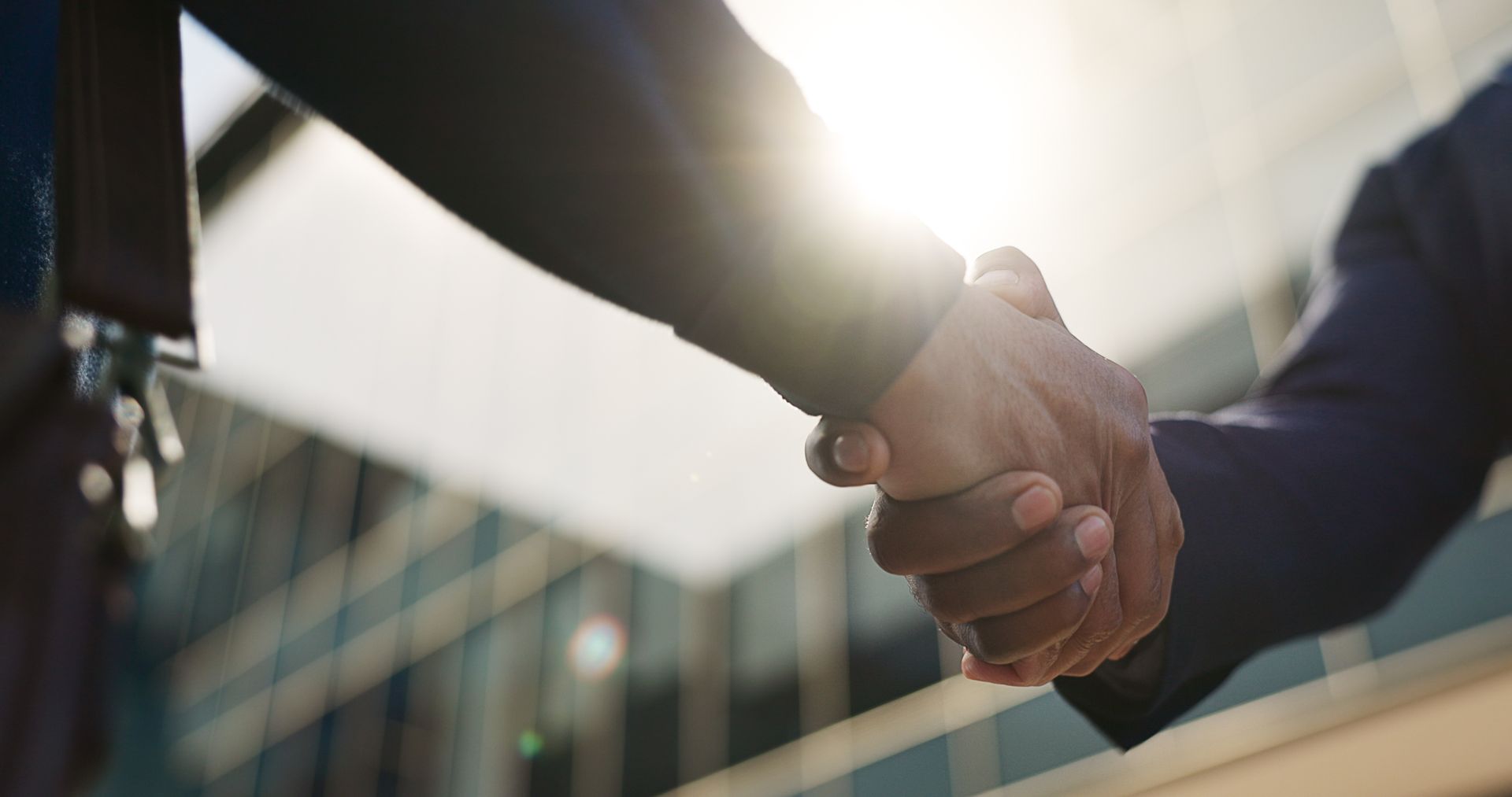 Two people shaking hands in a bright office setting with sunlight flare