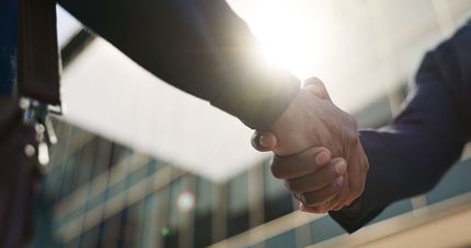 Two people shaking hands in a bright office setting with sunlight flare