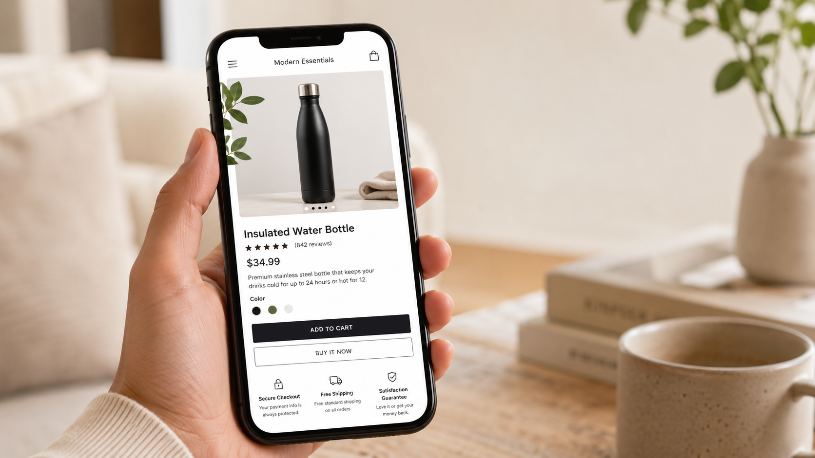 Hand holding a smartphone showing a black bottle product page on a wooden table with a cup and books nearby