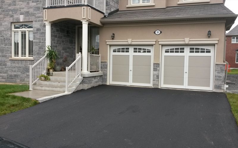 A house with two garage doors and a black driveway.