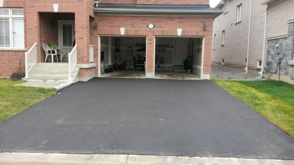 A driveway in front of a brick house with two garages.