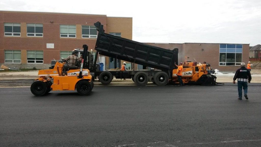 A dump truck is being loaded with asphalt in front of a brick building