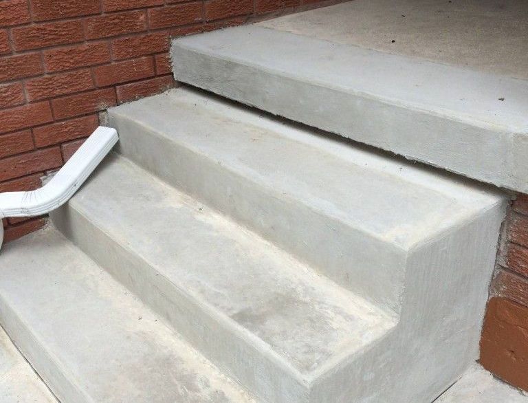 A set of concrete stairs with a white railing next to a brick wall.
