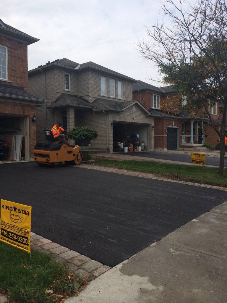 A group of people are working on a driveway in front of a house.