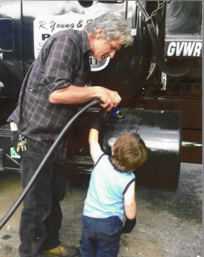 Man and child washing a black truck. The man holds a hose, while the child points at the water stream.
