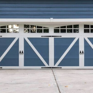 Blue garage door with white trim, arched windows, and decorative black hardware against a concrete driveway.