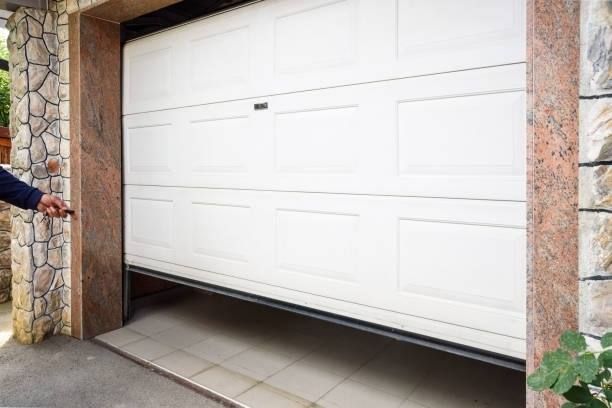 A white sectional garage door is partially open, showing the tiled floor inside, with a person's hand visible near the frame.