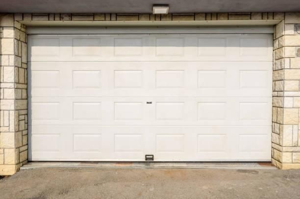 A white, multi-panel garage door framed by stone walls with a small overhead light fixture.