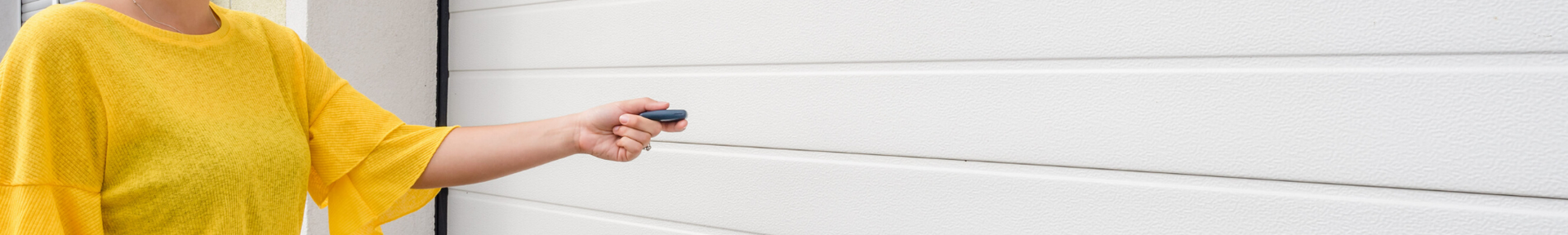 A person in a yellow shirt points a garage door remote at a white panel garage door.