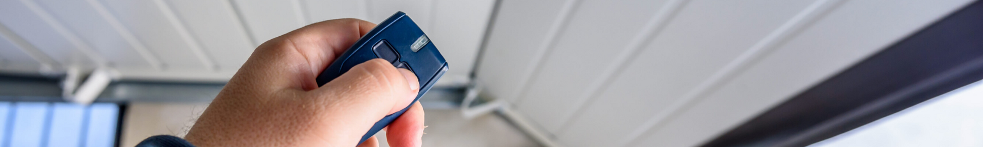 A hand presses a button on a small, dark remote control, likely to open or close a garage door.