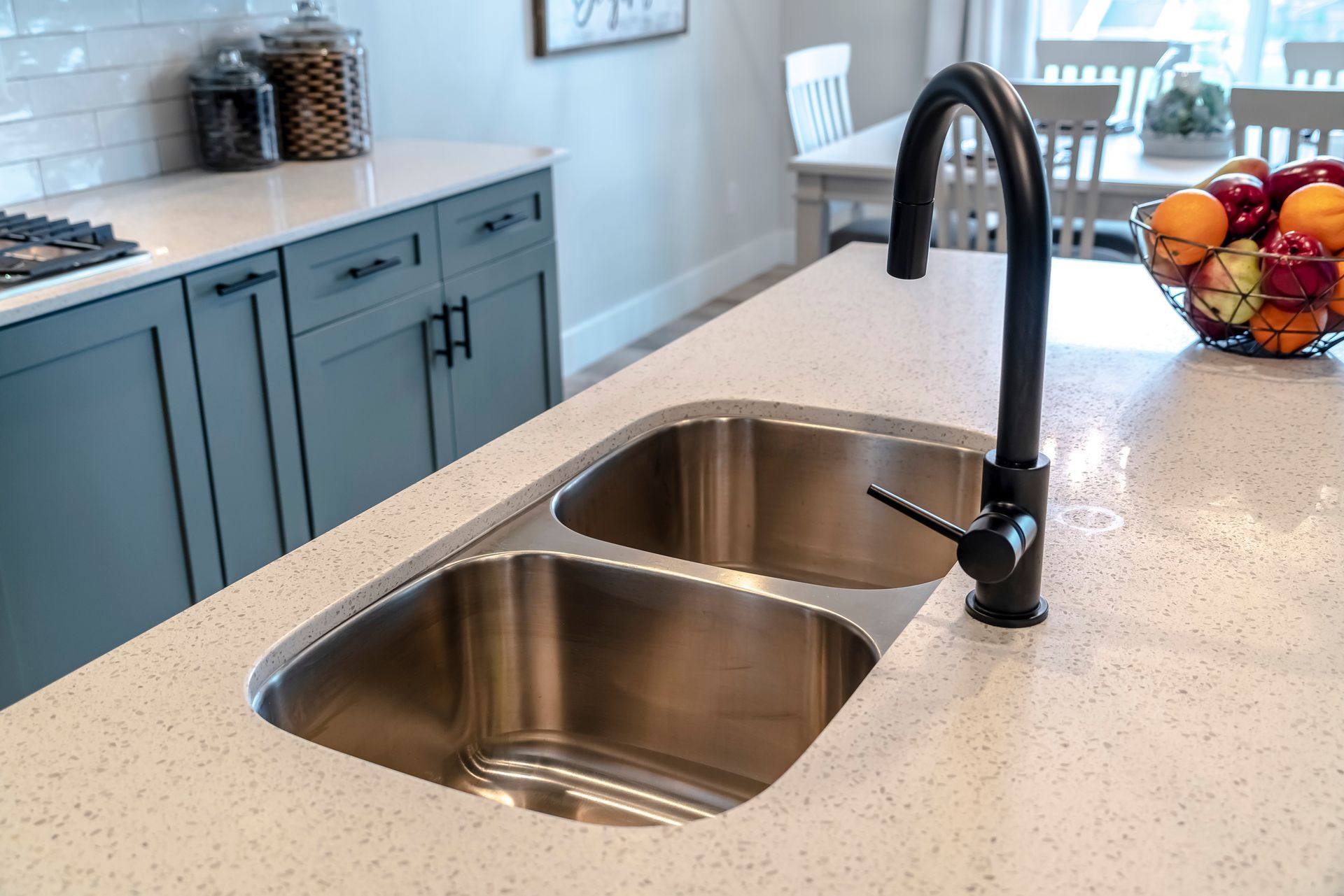 A kitchen sink with a black faucet and a bowl of fruit on the counter.