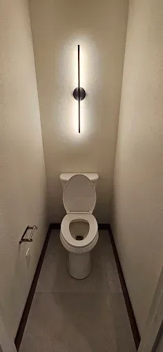 A toilet in a small bathroom with a light on the wall.