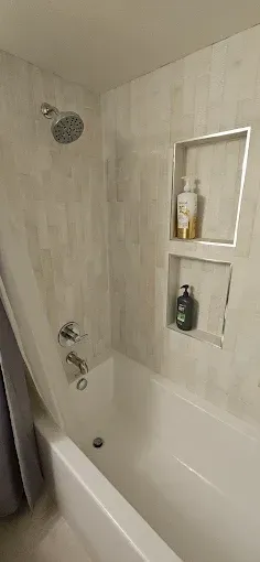 A bathroom with a bathtub , shower , and soap dispenser.