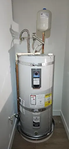A water heater is sitting in a corner of a room next to a wall.