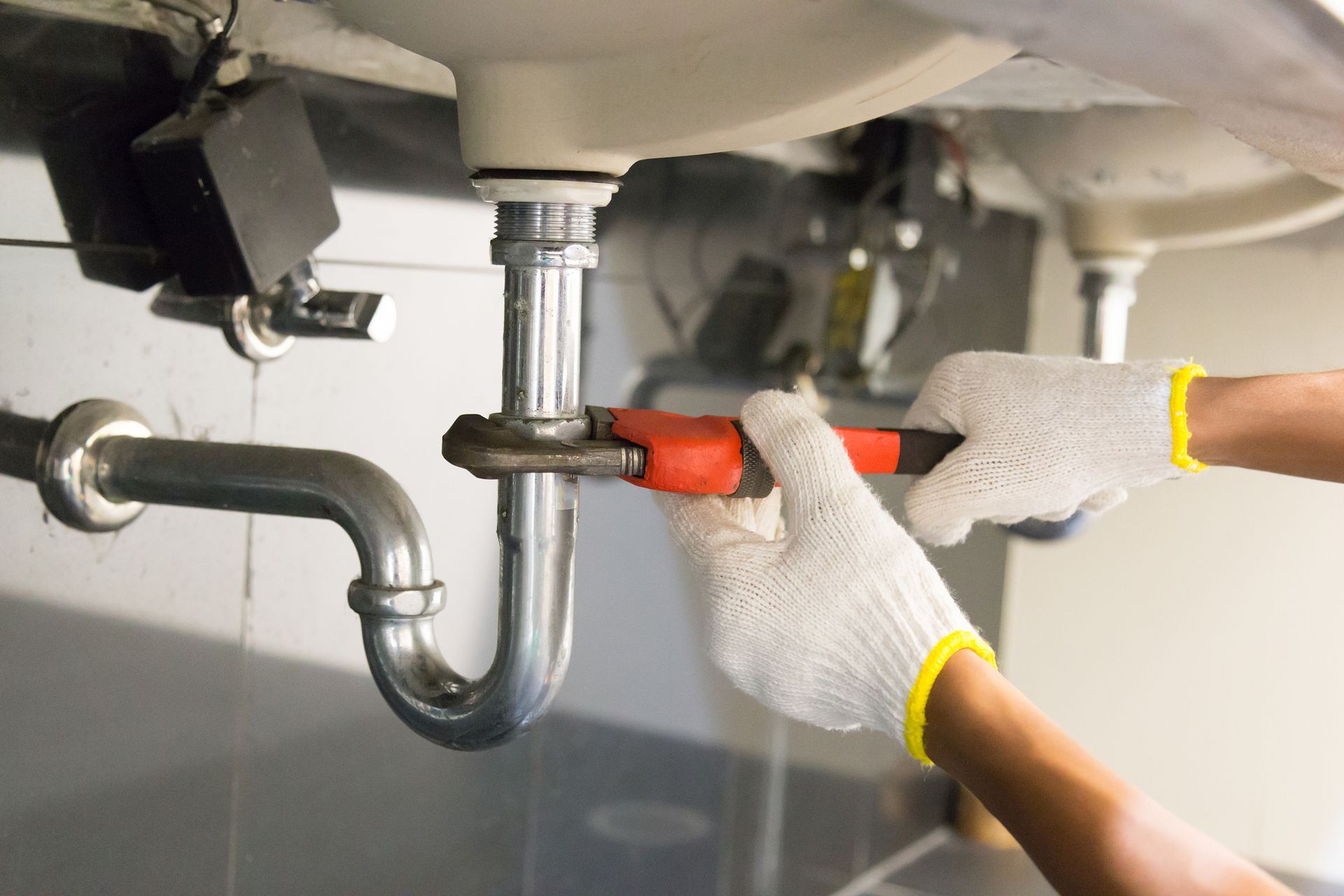A plumber is fixing a sink pipe with a wrench.
