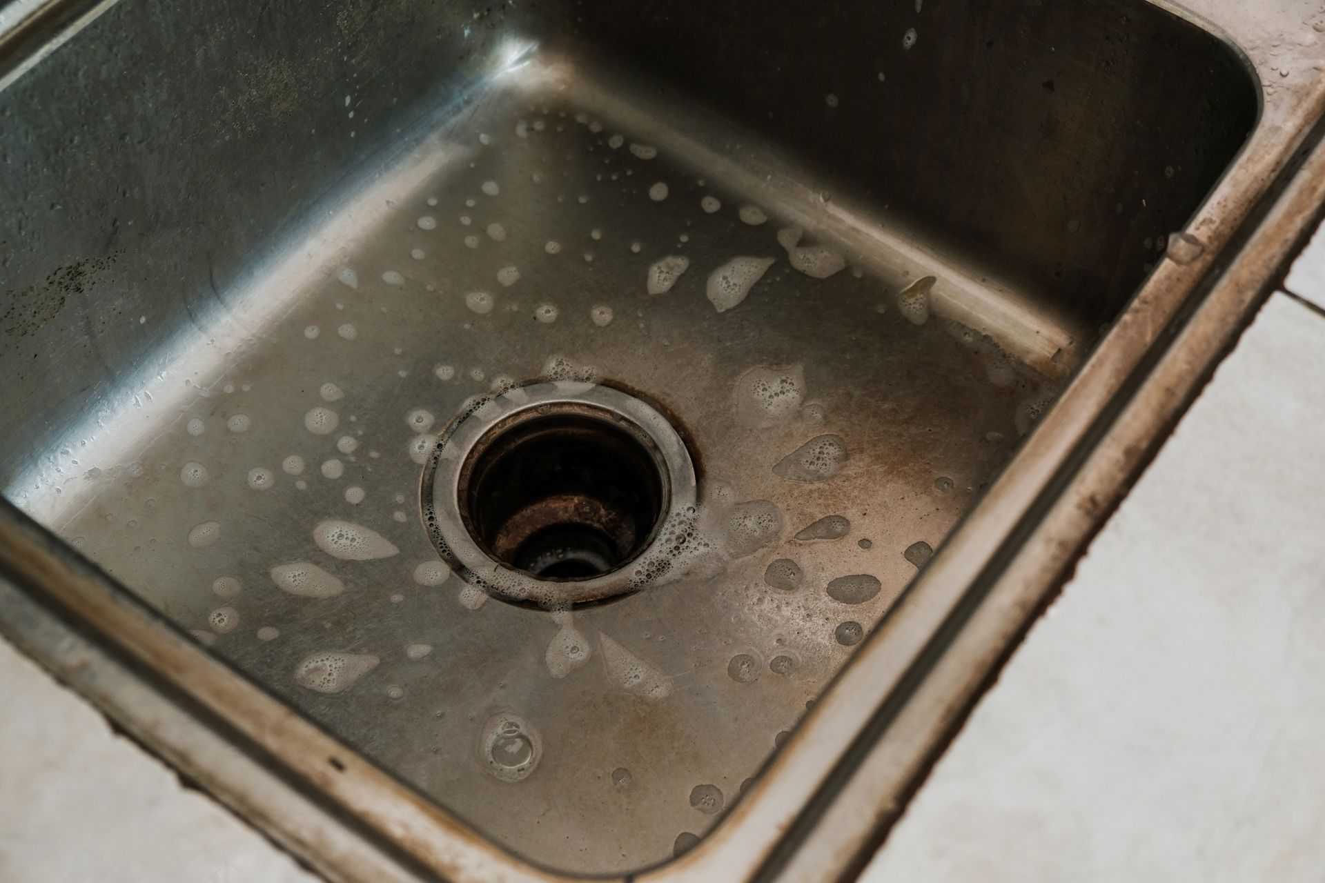Stainless steel kitchen sink with soap residue around the drain.