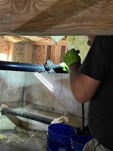 A man is spraying foam on a pipe in a basement.