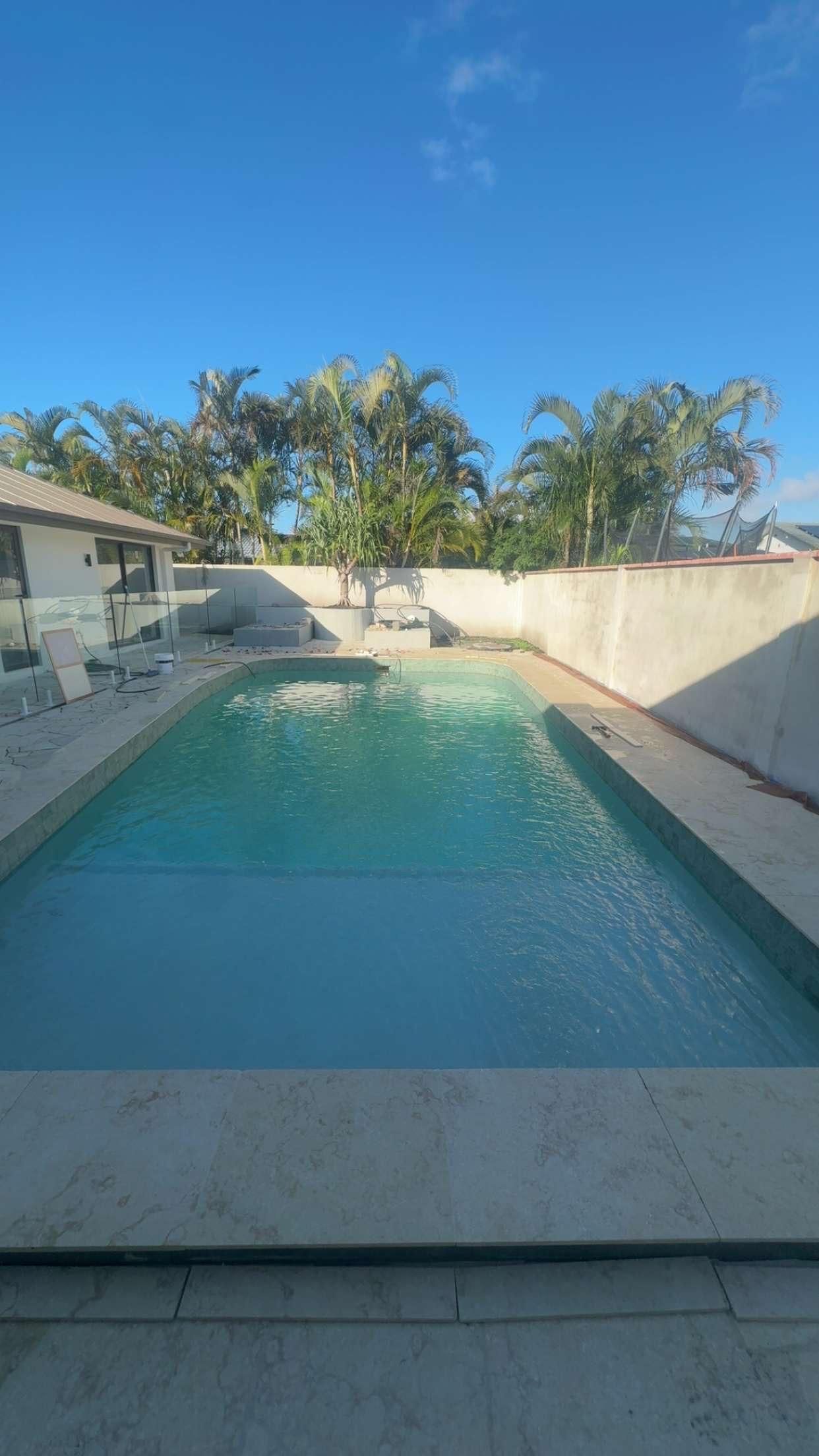 Backyard swimming pool with turquoise water, white walls, and palm trees under a bright blue sky